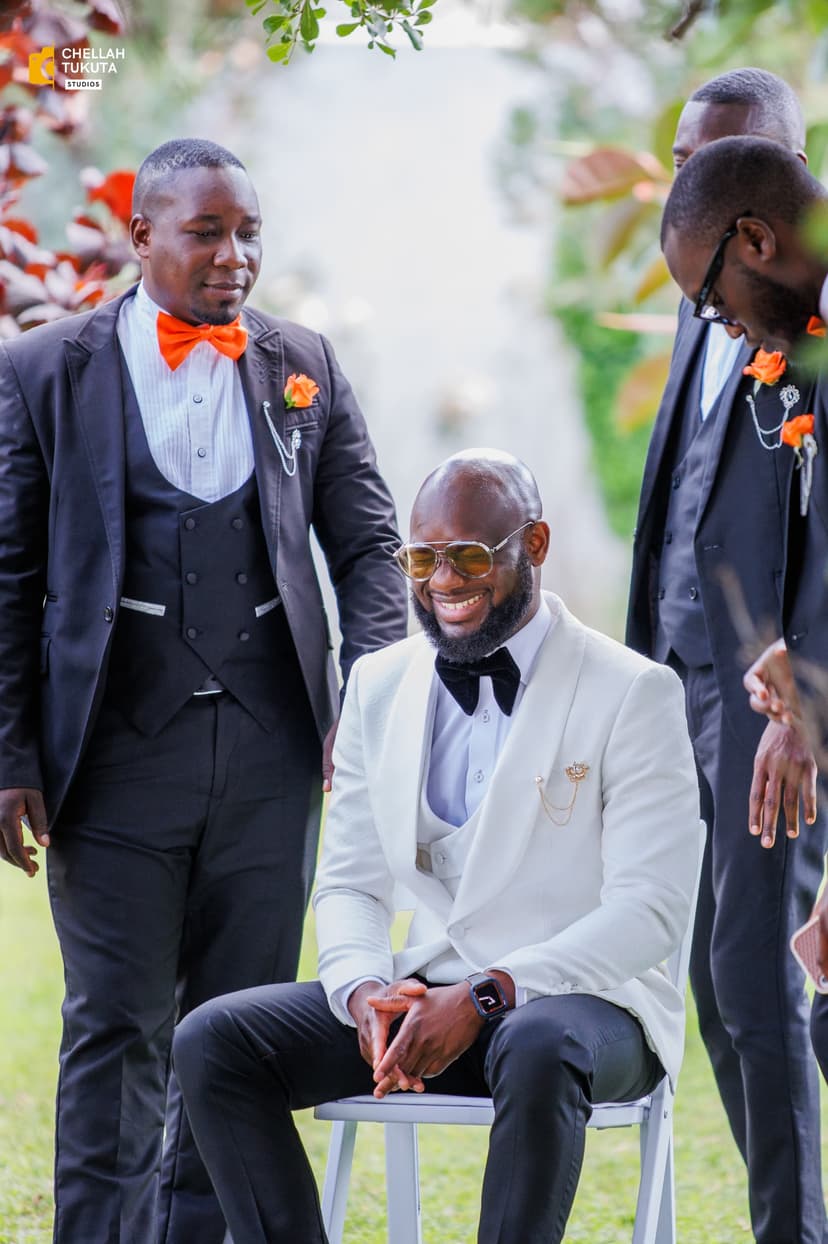 Groom in white suit with groomsmen in dark suits with orange accents