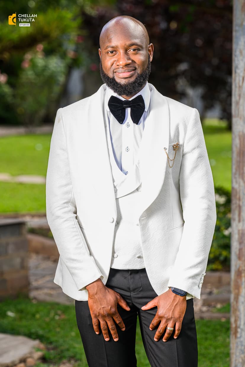 Elegant groom portrait in white three-piece suit in garden