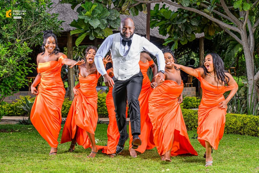 Fun bridal party photo with groom jumping surrounded by bridesmaids in orange