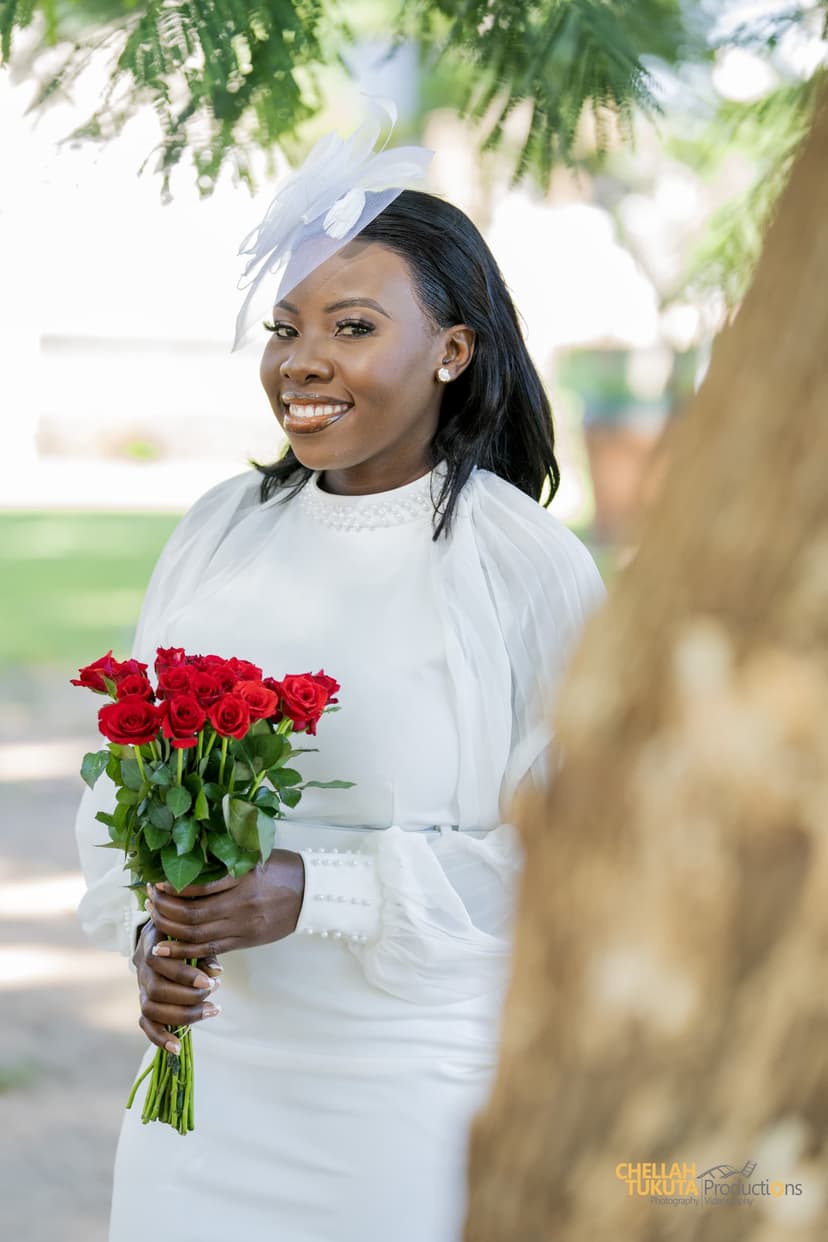 Bride in white dress with fascinator holding red roses in garden
