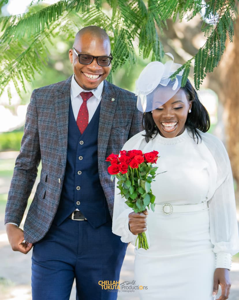 Happy couple walking - groom in checkered suit, bride with fascinator and red roses