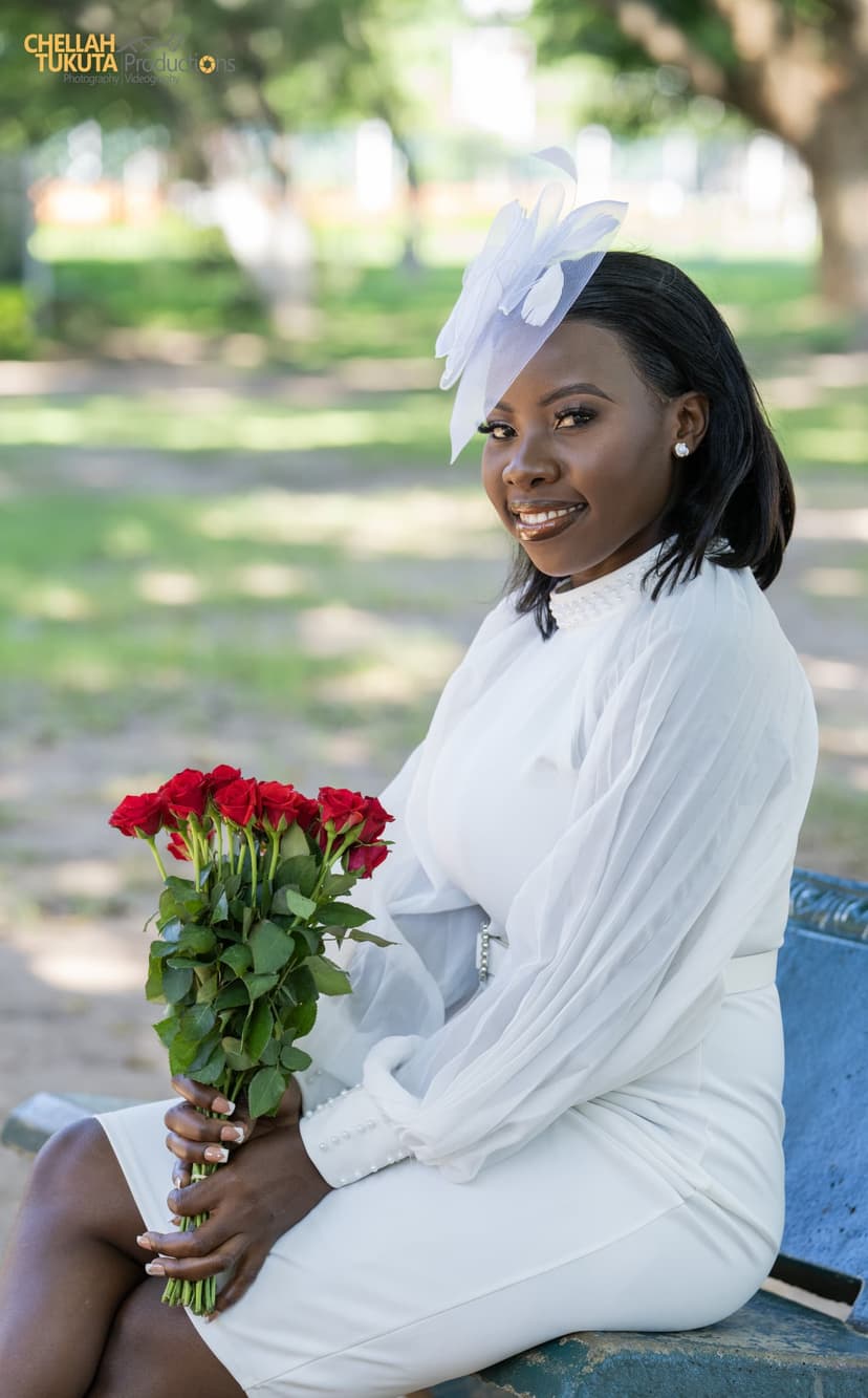 Bride seated portrait in white dress with fascinator holding red roses