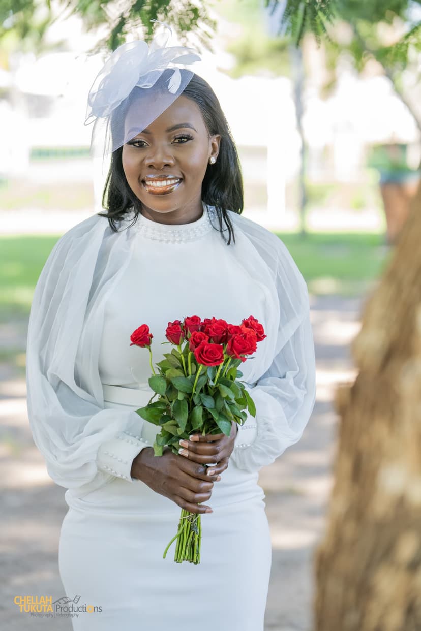Full length bridal portrait in white dress with fascinator and red roses