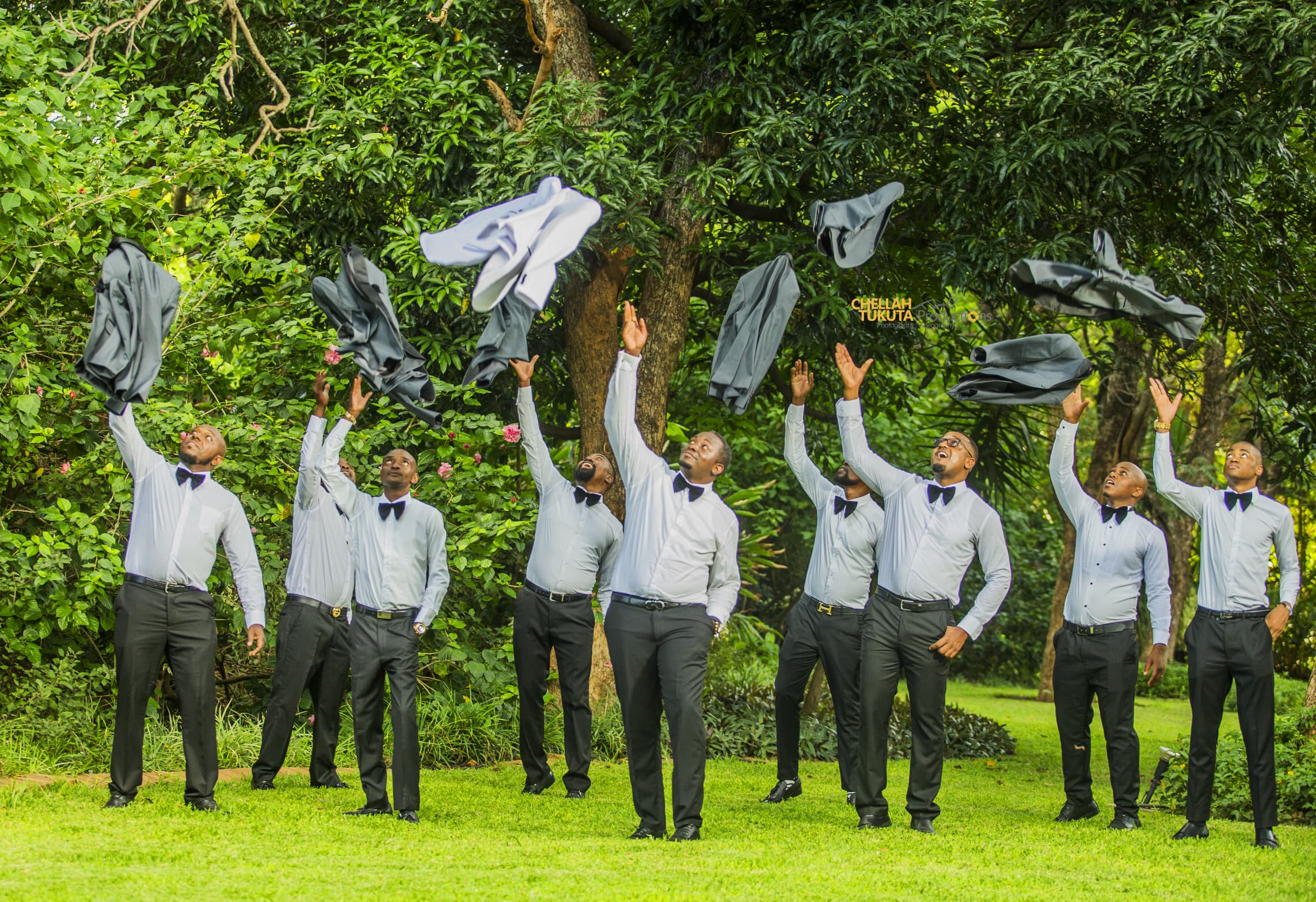 Fun groomsmen celebration - throwing suit jackets in the air in garden setting