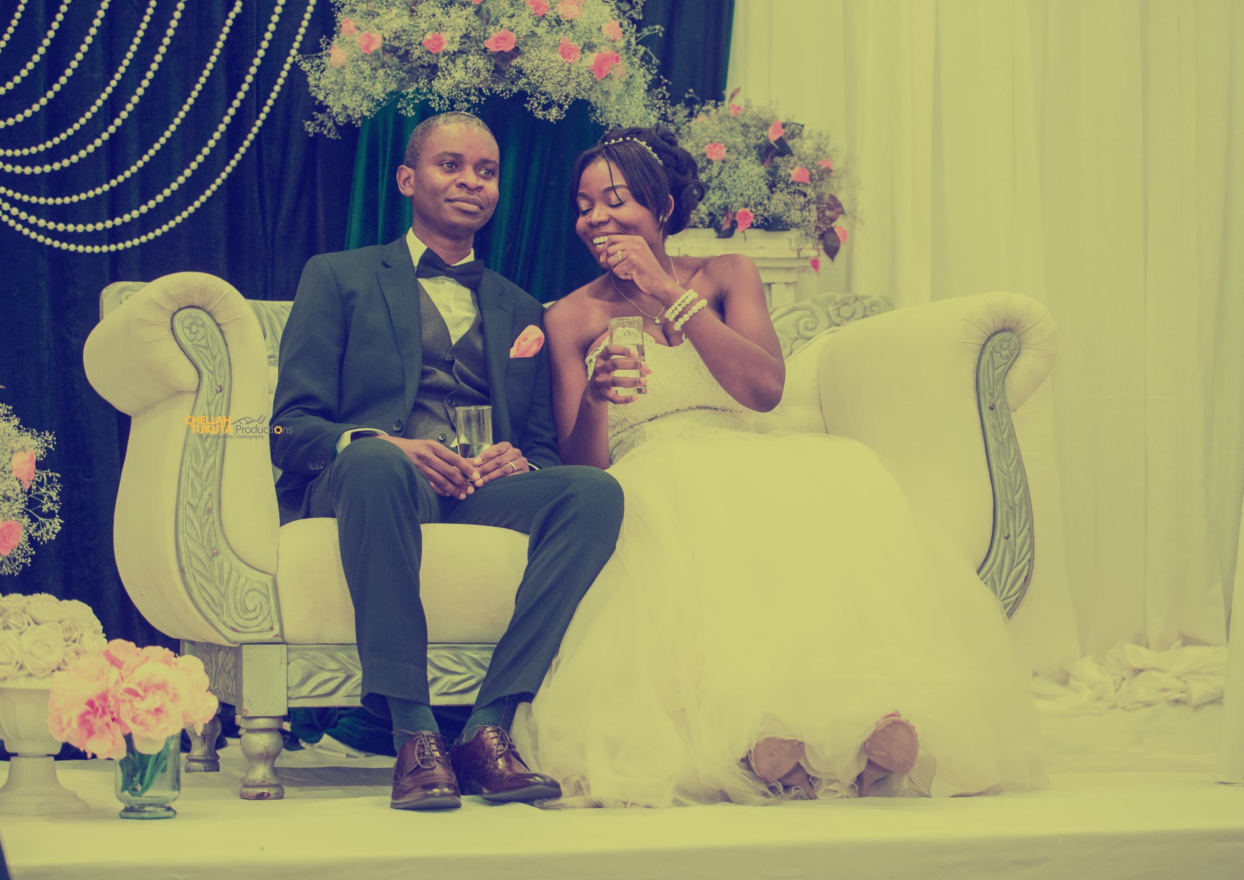 Luxury reception moment - couple on ornate white sofa with champagne and floral backdrop
